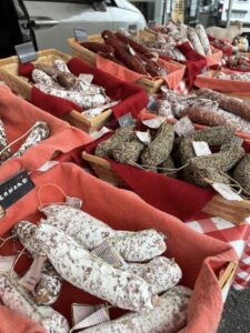 Stand de vente de charcuterie sur le marché en plein air hebdomadaire. A Val d'Anast, rendez-vous chaque dimanche matin sur la Place Arthur Regnault pour rencontrer les artisans et commerçants locaux.