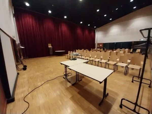 La Salle du Rotz est disponible à la location pour les particuliers, professionnels et associations. Elle est équipée d'une scène, d'un parquet et de gradins. Aussi, elle bénéficie de nombreux espaces complémentaire réservables : hall d'accueil, bar, cuisines, sanitaires et vestiaires. Sur cette photo se trouve la salle disposée pour un séminaire. Prendre contact avec le Pôle Evénementiel via le formulaire de pré-réservation des salles communales.