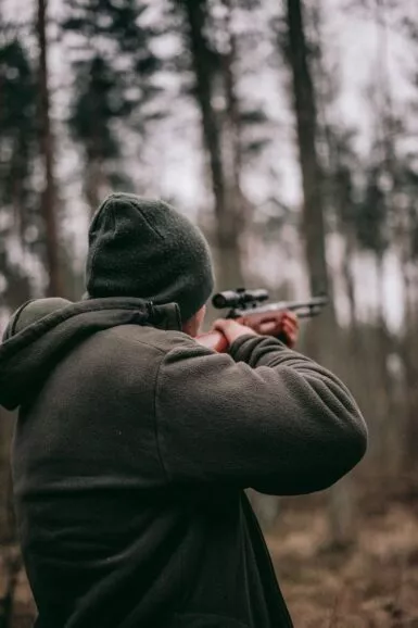Chasseur pointant son fusil en direction de la forêt
