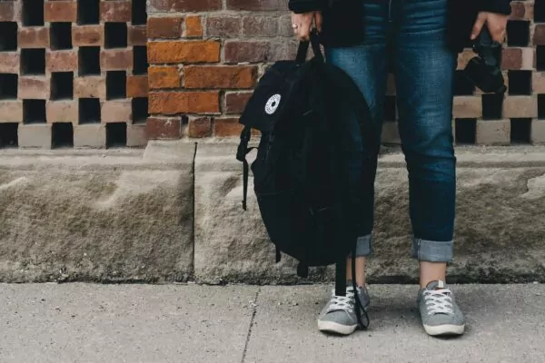 Personne patientant sur le bord d'un trottoir, vraisemblablement sortant d'une journée de cours à l'école, au collège ou au lycée.